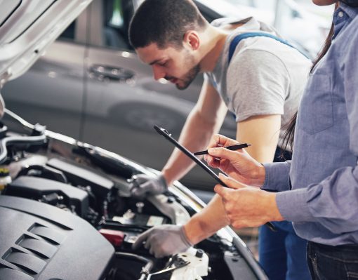 A man mechanic and woman customer look at the car hood and discuss repairs.